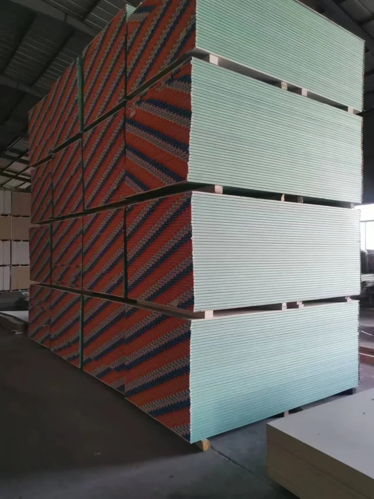 Large stack of drywall panels with striped packaging stored in an industrial warehouse setting.