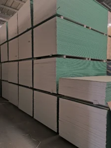 Large stacks of drywall sheets with green edges arranged neatly in a warehouse setting.