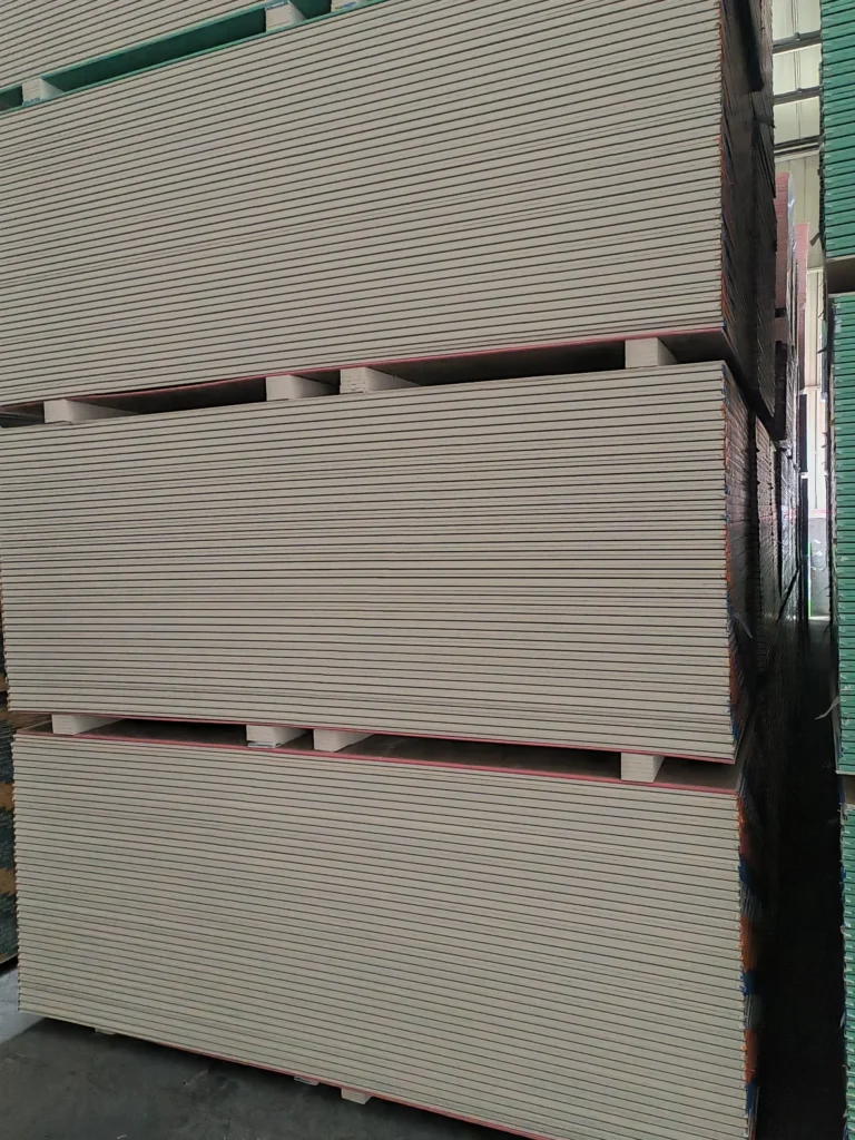 Large stacks of drywall panels stored in a warehouse, showing organized rows and industrial shelving.