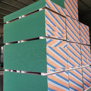 Large stack of green drywall panels stored in a warehouse along with panels wrapped in blue and orange packaging.