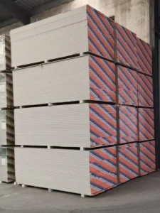 Tall stacks of drywall sheets placed neatly in a warehouse, with colorful striped edges visible, indicating orderly storage.