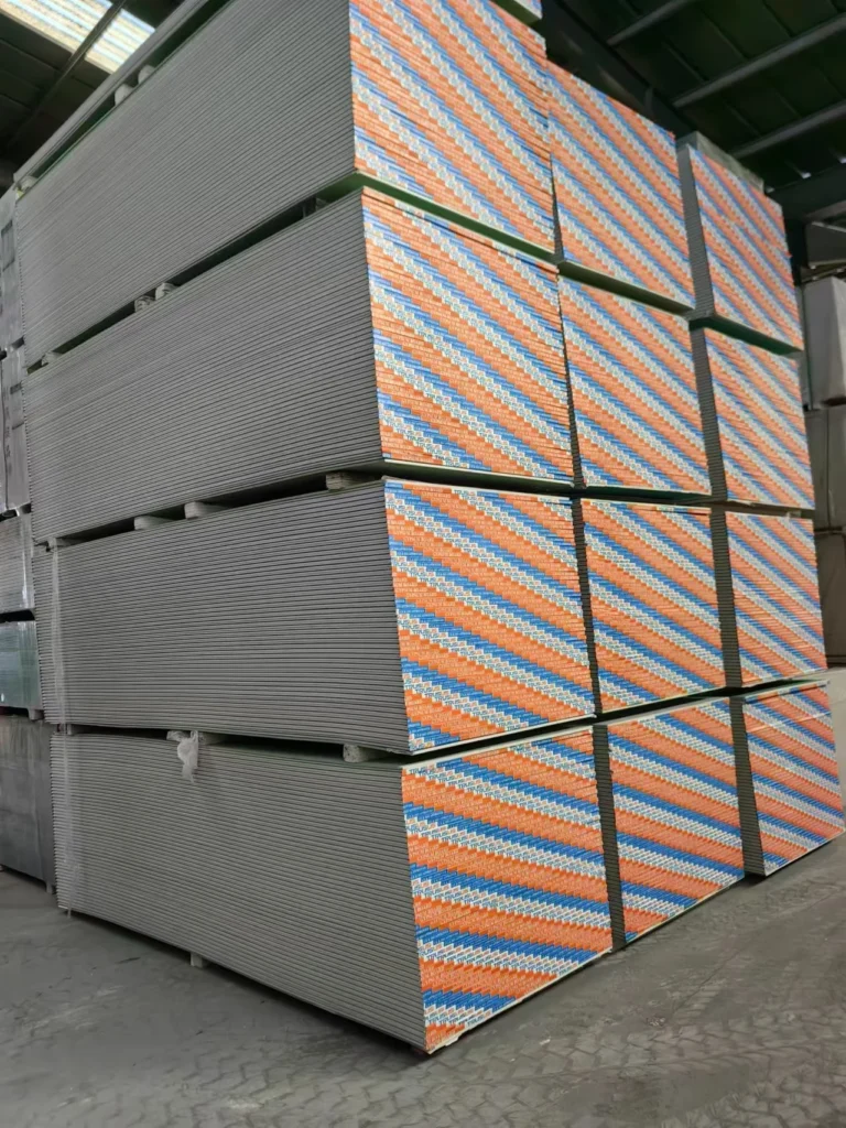 Large stacks of fiber cement boards with striped edges, organized in a warehouse setting.