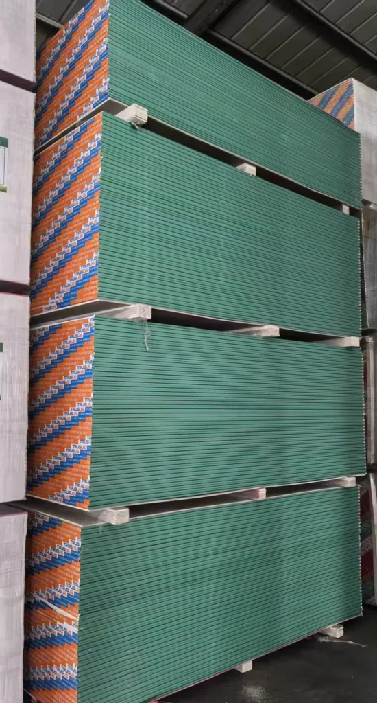 Large stack of green drywall panels neatly arranged in a warehouse setting, secured and ready for shipment.