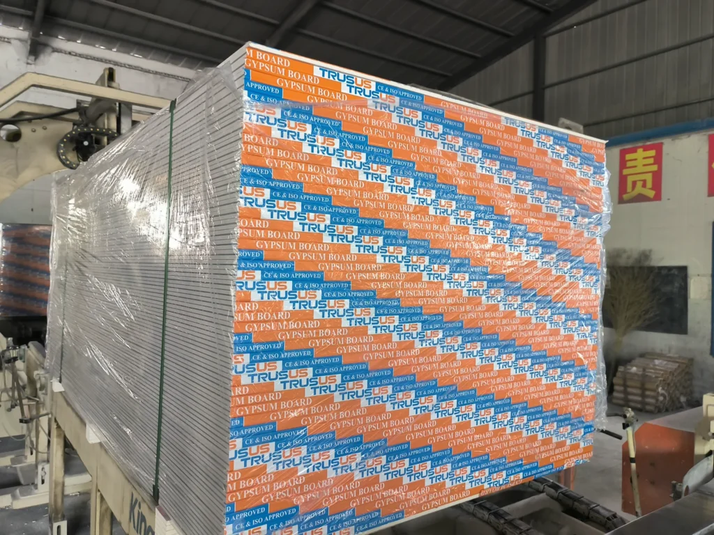 Stack of TRUSUS gypsum boards wrapped in plastic at a warehouse, showing packaging and storage.