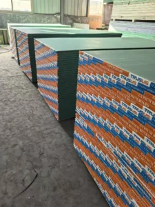 Piles of gypsum boards stacked neatly in a warehouse, with labels visible on the side and ample natural light from windows.