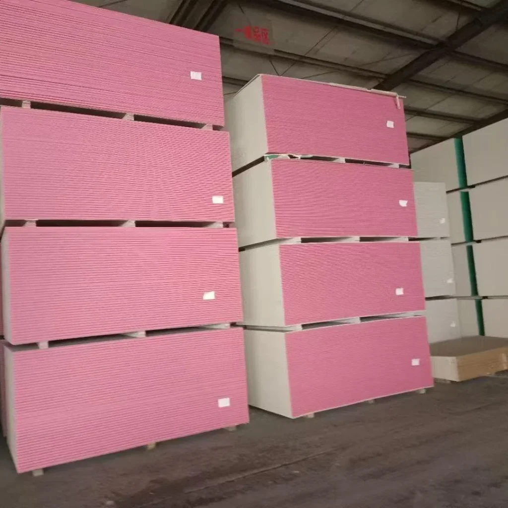 Rows of pink drywall sheets stacked neatly in a warehouse interior with visible ceiling beams and concrete floor.