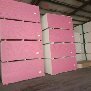 Rows of pink drywall sheets stacked neatly in a warehouse interior with visible ceiling beams and concrete floor.
