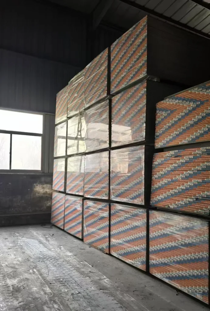 Stacks of plywood sheets wrapped in packaging in a dimly lit warehouse with a large window.