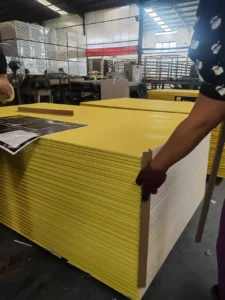 Stacked yellow panels being handled in an industrial factory environment with various machinery and equipment visible.