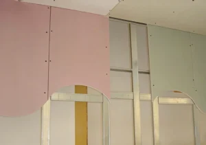 Pink and green drywall panels partially installed on a metal frame, showing curved designs and construction progress.