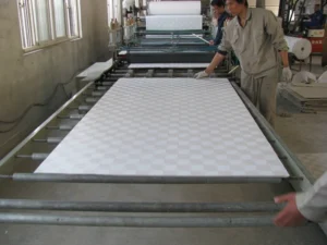 Two workers monitoring a fabric production line with patterned fabric in a factory setting.