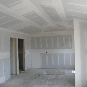 Room under construction with installed drywall, showing unpainted walls, ceiling, and unfinished floor.