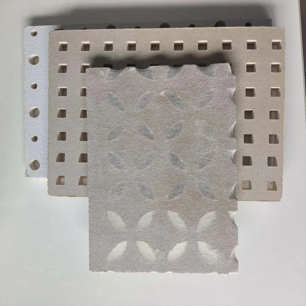 Three textured paper sheets layered on a white surface, featuring square cut-outs and decorative floral patterns.